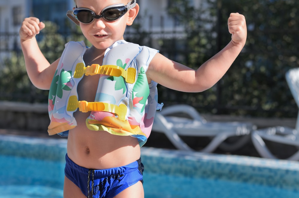 Photo of a young boy wearing a colorful safety pool vest with black goggles in a funny pose.